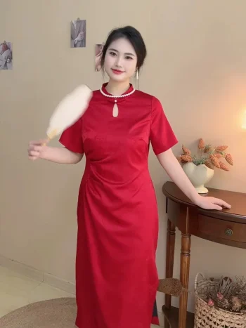 Plus size woman in a smooth red satin qipao dress, form-fitting chinese red qipao with subtle floral jacquard pattern and short sleeves, posing casually in a cozy living room with soft lighting.