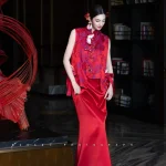 Red Silk Qipao Set - Woman in modern red qipao set with brocade vest and trailing satin mermaid skirt, standing in a luxury hotel lobby with a bookshelf backdrop, elegant two-piece chinese qipao for wedding photoshoots