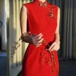 Red Modern Modified Sleeveless Long Wedding Qipao Dress - Close-up of the elegant mandarin collar and floral embroidery details on a sleeveless red qipao wedding dress. The bride holds a flower branch in soft backlit light, highlighting the delicate craftsmanship and refined design of this modern qipao for weddings.