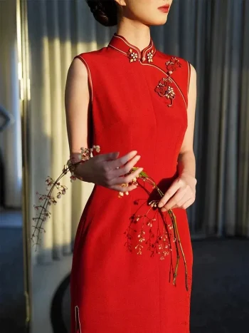 Red Modern Modified Sleeveless Long Wedding Qipao Dress - Close-up of the elegant mandarin collar and floral embroidery details on a sleeveless red qipao wedding dress. The bride holds a flower branch in soft backlit light, highlighting the delicate craftsmanship and refined design of this modern qipao for weddings.