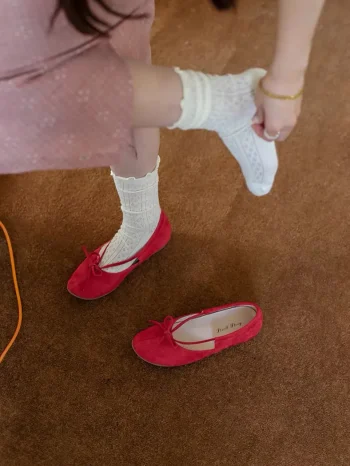 Red suede Mary Jane qipao shoes with white lace knit socks on feet, shown on a warm brown carpet for a cozy, vintage-inspired everyday style