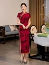 Full-length view of a woman in red vintage floral qipao with gold trim, showcasing traditional cheongsam design in a modern Chinese interior.