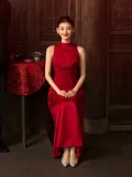 A bride sits gracefully in a traditional Chinese wooden interior, wearing a sleeveless red wedding cheongsam dress with a high neckline. This elegant cheongsam wedding dress features a timeless silhouette perfect for Chinese wedding ceremonies and photoshoots.