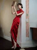 Side view of woman in a red satin qipao dress with intricate floral embroidery on sheer lace sleeves, form-fitting wedding qipao with draped skirt and high slit, posing with a book against a wall.