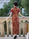 Back view of a woman standing on a stone balcony railing, wearing a 1930s reddish-brown floral silk qipao, showcasing the full floral print pattern, high mandarin collar, and flowing hem from the rear.