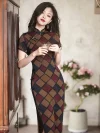 Women's retro checkered cheongsam in warm earthy tones, a classic qipao with a geometric plaid pattern, short sleeves, and a refined stand-up collar. The model leans on a vintage wooden cabinet holding a glass cup, showcasing the rich texture of the premium fabric.