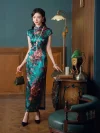 Retro green silk qipao for women with peony print, model standing by antique desk, showing elegant traditional dress design