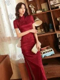 Woman in retro red rose print long cheongsam prom dress, elegant women's cheongsam dress with traditional mandarin collar and high slit, posing in a vintage-style room with wooden bookshelf decor.