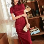Woman in retro red rose print long cheongsam prom dress, elegant women's cheongsam dress with traditional mandarin collar and high slit, posing in a vintage-style room with wooden bookshelf decor.