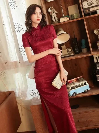Woman in retro red rose print long cheongsam prom dress, elegant women's cheongsam dress with traditional mandarin collar and high slit, posing in a vintage-style room with wooden bookshelf decor.