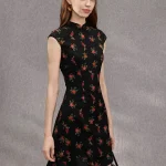 Woman wearing a summer black base rose print sleeveless short qipao dress, standing in profile to show the slim fit silhouette and classic mandarin collar.