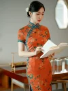 Old Shanghai style tangerine red peony print long cheongsam (qipao) with blue trim, elegant women's traditional dress, model standing and reading a book.
