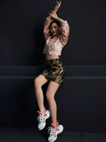 Full-body shot of a woman styling the ink black tiger jacquard A-line short skirt with a pink traditional top and sneakers, highlighting the skirt's high waist and vibrant tiger jacquard pattern; versatile black short skirt for casual-chic looks