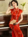 Model wearing a traditional Chinese wedding red long qipao, seated on a vintage piano with a folding fan, showcasing the elegant satin fabric and delicate floral print.