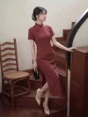 Women's 1940s traditional red plaid qipao dress, a timeless red qipao with a classic checkered pattern, short sleeves, stand-up collar, and high slit. The model poses on a wooden staircase holding a black clutch, leaning against a wooden cabinet to highlight the vintage-inspired design and elegant fit.