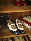 Two-tone black and white Margarita 1920s vintage schoolgirl leather Qipao shoes with rivet accents, displayed on a wooden shelf alongside other vintage footwear styles.