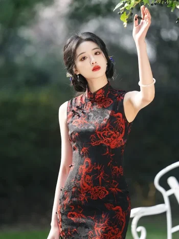 Close-up of women's vintage floral sleeveless high cut cheongsam with red dragon print on black fabric, model raising hand to touch tree leaves outdoors, showing fabric texture and print details.