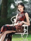 Vintage sleeveless high cut cheongsam (qipao) with bold red dragon and floral print on black fabric, elegant long qipao for women, model sitting on a white chair outdoors holding a small brown handbag.