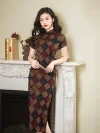 Women's vintage plaid short sleeve cheongsam with a high slit, featuring a bold geometric checkered pattern in brown, red, and blue. The model leans on a white fireplace mantel holding a folding fan, highlighting the dress’s elegant silhouette and timeless design.