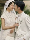 Vintage Modified White Lace Wedding Qipao Dress - Bride in a lace qipao with multi-layer pearl necklace and vintage handbag, posing closely with her groom, showcasing the delicate lace overlay and high collar, ideal for intimate wedding moments.