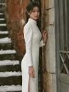 Vintage Modified White Lace Wedding Qipao Dress - Bride in a long-sleeve white lace qipao, leaning against a weathered stone wall with snow-covered steps, featuring a high mandarin collar with pearl details, intricate lace texture, and side slit, perfect for vintage-style bridal photoshoots and modern Chinese weddings.