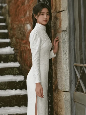 Vintage Modified White Lace Wedding Qipao Dress - Bride in a long-sleeve white lace qipao, leaning against a weathered stone wall with snow-covered steps, featuring a high mandarin collar with pearl details, intricate lace texture, and side slit, perfect for vintage-style bridal photoshoots and modern Chinese weddings.