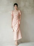 Wall-leaning view of women's summer modified cheongsam, new Chinese style long dress with square neck puff sleeve, waist cinched pleated design in soft pink textured fabric showing elegant drape