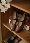 Warm Brown Margarita 1920s Vintage Schoolgirl Style Leather Qipao Mary Jane Shoes, displayed on a wooden shelf with white orchids, featuring classic brogue detailing for retro cheongsam style.