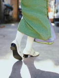 Back view of white 1920s Qipao dress goat leather shoes with cutout details, worn with a green vintage cheongsam while walking outdoors, highlighting the classic heel design.