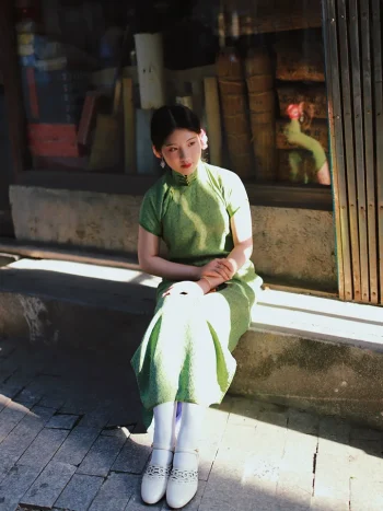 White 1920s Qipao dress goat leather shoes with delicate cutout details, paired with a vintage green cheongsam, worn by a model sitting on outdoor stone steps, capturing old Shanghai aesthetic.