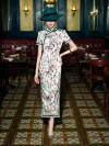 Full-body shot of a model in a Chinese silk qipao dress with white floral print, standing with hands on hips in a classic restaurant, highlighting the traditional frog buttons and elegant cut.