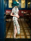 Side view of a woman in a Chinese silk qipao dress with white base and pink floral print, wearing a green hat and showing the high slit design in a retro restaurant.