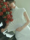 White Lace Fishtail Wedding Cheongsam Dress - Close-up of a bride in a lace cheongsam wedding dress, leaning against a piano with red roses, holding a lace fan. The white lace cheongsam features intricate lace details, a high mandarin collar, and short sleeves, perfect for elegant wedding photos and bridal prep moments.
