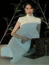 White Lace Fishtail Wedding Cheongsam Dress - Woman in a white lace cheongsam with fishtail silhouette, sitting on the floor in a traditional Chinese setting with bamboo and calligraphy scrolls. The lace cheongsam features a high collar, short sleeves, and delicate lace texture, holding a lace fan for a vintage-inspired bridal look.