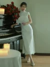 White Lace Fishtail Wedding Cheongsam Dress - Full-body shot of a woman in a white lace fishtail cheongsam wedding dress, leaning against a grand piano with red roses and candles. The lace cheongsam features a form-fitting silhouette, lace trim, short sleeves, and side slit, creating a romantic bridal look for wedding day and formal events.
