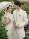 White Qipao Wedding Dress - Close-up of bride in a vintage white lace qipao, holding a lace parasol while posing with her groom in a white suit, highlighting the intricate lace patterns and classic mandarin collar, perfect for romantic wedding photoshoots.