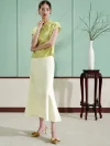 Full-body shot of a woman styling a light green modern Chinese mulberry silk cheongsam shirt with a cream mermaid skirt, showcasing the versatile design of this short sleeve qipao top for formal and casual occasions.