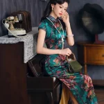 Model wearing vintage green printed silk long qipao seated on piano in retro room, elegant traditional Chinese dress with peony print