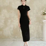 A woman wearing a black slim fit qipao dress stands facing the camera. This elegant women qipao features a classic stand collar with a keyhole cutout, side drawstring detail, and a flowing silhouette.