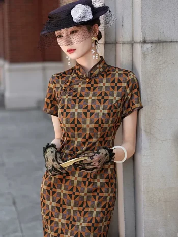 Side view of a women's checkered long cheongsam, an Old Shanghai style qipao dress. The model leans against a stone wall, holding a wooden hand fan, showcasing the tailored silhouette, high stand-up collar, and intricate checkered pattern in rich brown, black, and warm tones, styled with lace gloves and period jewelry.