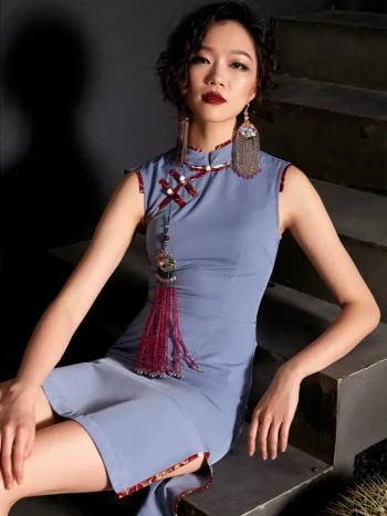 Elegant woman seated on concrete stairs wearing a misty blue short cheongsam dress with traditional red frog buttons and pink tassel accessory, a modern take on women's cheongsams qipao.