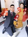 Yellow Modern Cheongsam Wedding Dress - Bride in chinese cheongsam posing with groom holding red envelopes, traditional wedding ceremony qipao with brocade texture and pearl details