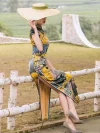 Side view of a model in a women high end yellow mulberry silk cheongsam dress with landscape print, sitting on a fence to highlight the high slit design and flowing drape.