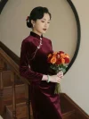 Elegant oriental lady wears tailored Velvet Long Sleeve Burgundy Cheongsam decorated with silver butterfly frog buttons, holding fresh red-orange roses beside solid wood staircase and round hollow wall frame, premium soft Cheongsam Velvet long sleeve cheongsam for retro formal outfit