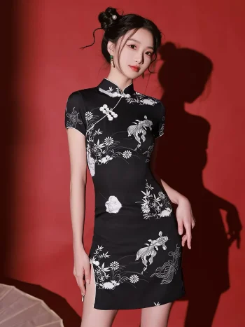 Woman modeling a black mini cheongsam dress with white floral and fish embroidery in a red studio.