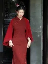 Sophisticated lady wearing a red long sleeve qipao paired with a matching lace-trimmed shawl, exuding traditional elegance in a classic outdoor setting.