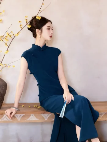 The seated view of a casual blue qipao outfit, model relaxing on a wooden bench, holding a folding fan beside blossoming yellow branches.