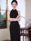 Stylish woman in an elegant black halter qipao with a chic pearl neck detail, standing with her arms crossed against a bright minimalist window setting.
