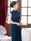 Profile shot of a model wearing an elegant blue cheongsam for casual wear, standing gracefully with a folding fan in a room with red curtains and wood doors.