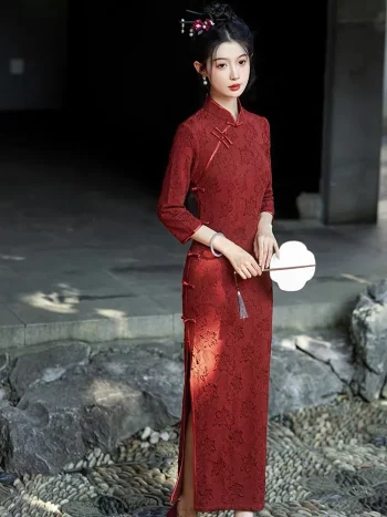 A refined lady modeled in a classic long sleeve qipao dress with elegant side slits, holding a delicate fan and standing gracefully on a stone-embedded pathway.